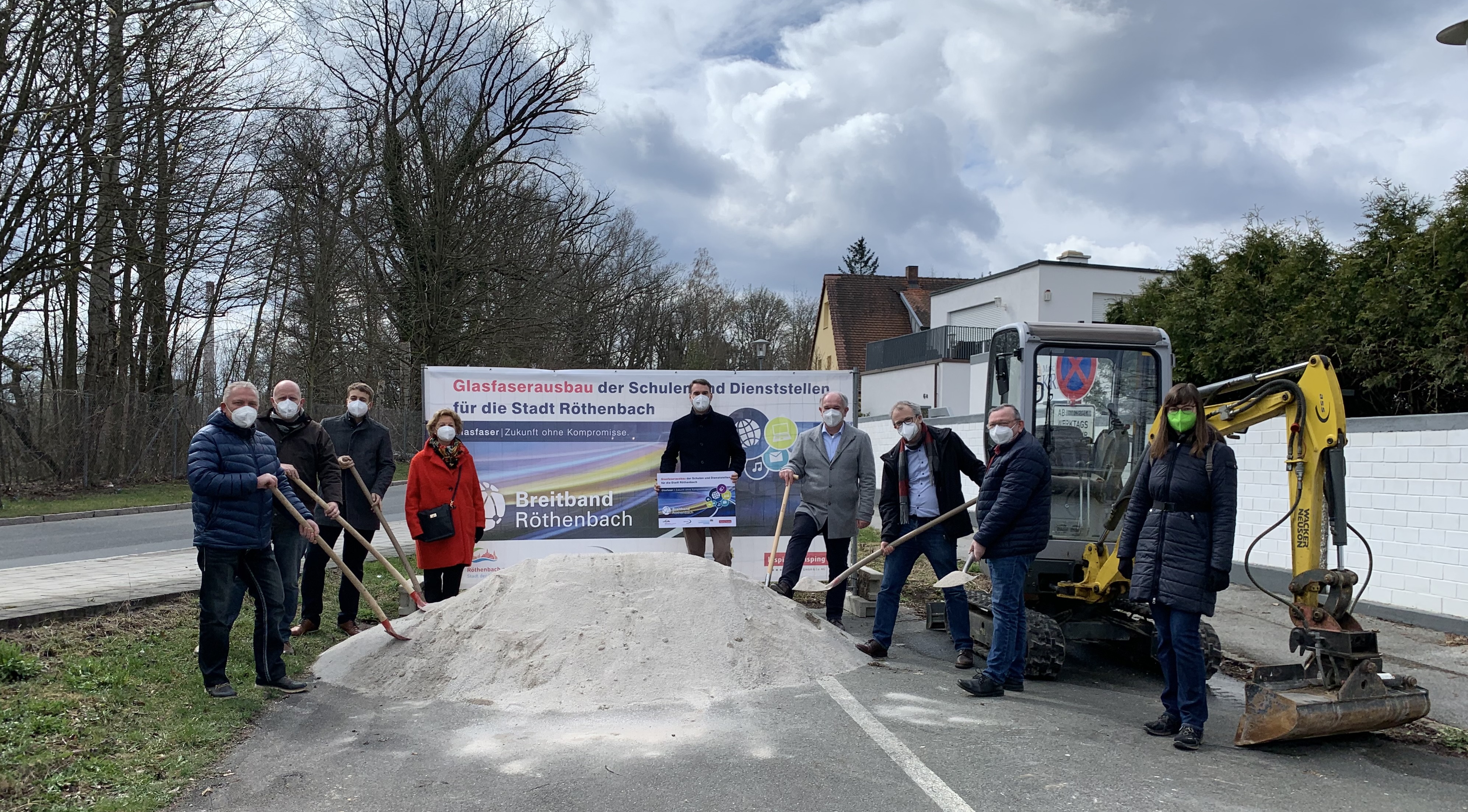 Symbolischer Spatenstich zum Glasfaserausbau der Schulen und Dienststellen in Röthenbach an der Pegnitz: Vertreter der Stadt, Bauunternehmen und Bisping & Bisping stehen mit Spaten vor einem Bagger und Sandhügel – ein gemeinsamer Schritt in Richtung digitale Zukunft.